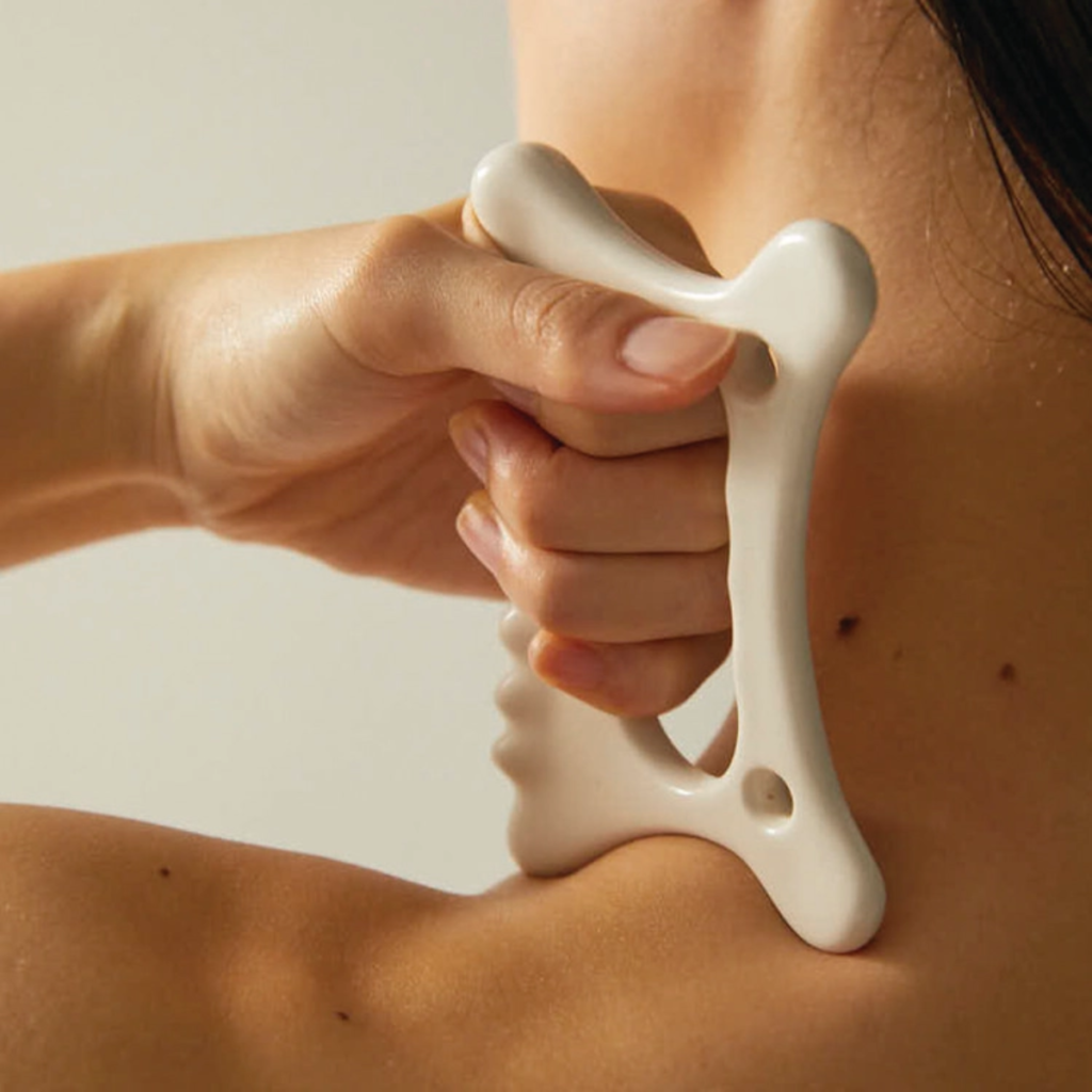 A woman using a gua sha on her shoulders